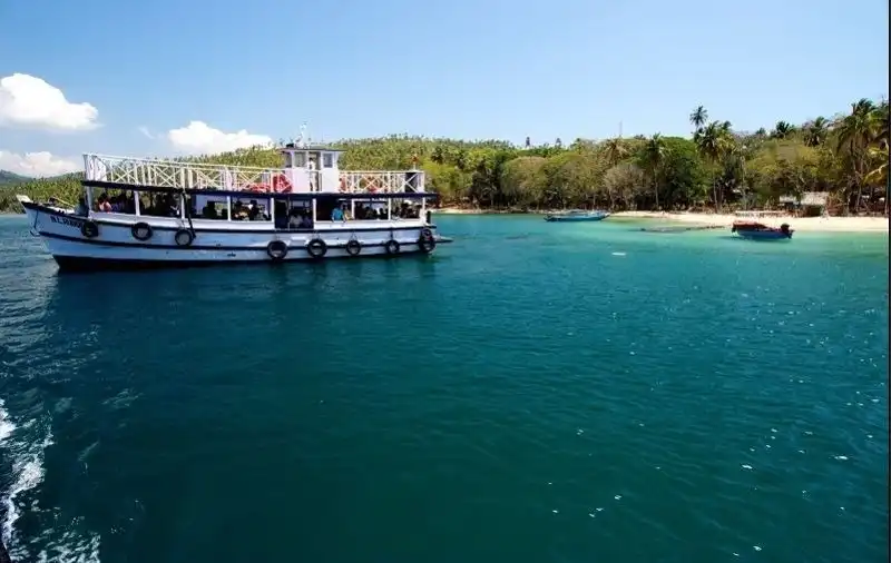 A large white boat navigates through clear blue waters near a tropical shoreline.